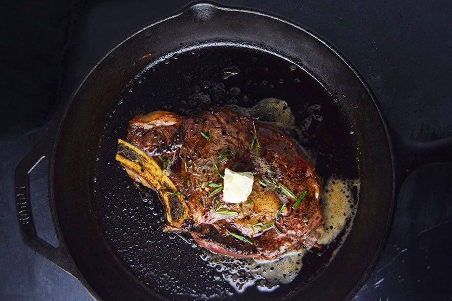 Large Prime Ribeye Steak Cooking on Black Skillet