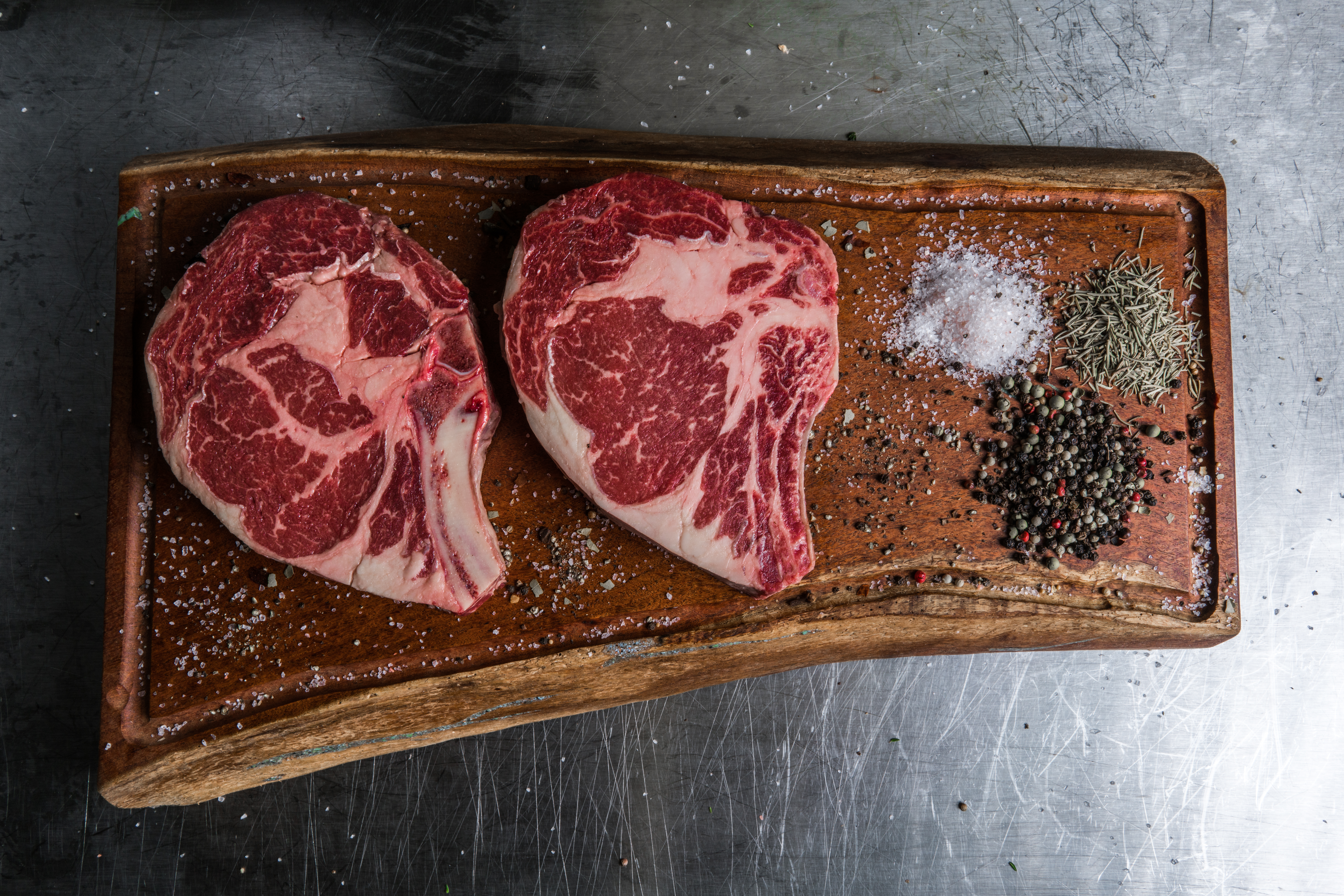 two prime steaks with herbs on a crafted wood chopping board