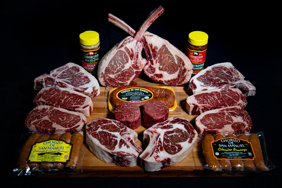 Uncooked prime steaks on a table with black background from chorizo de san manual, and several packages of the best chorizo brand.