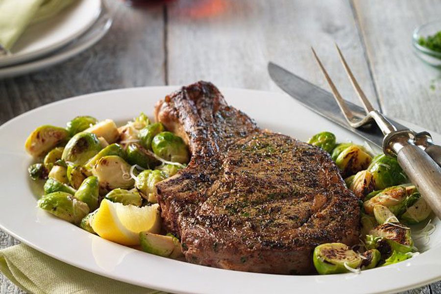 White plate decorated with roasted brussel sprouts and a thick cut of ribeye steak.
