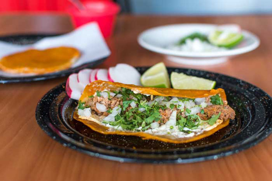 Black platter of brisket tacos made with prime beef products on a wooden table.