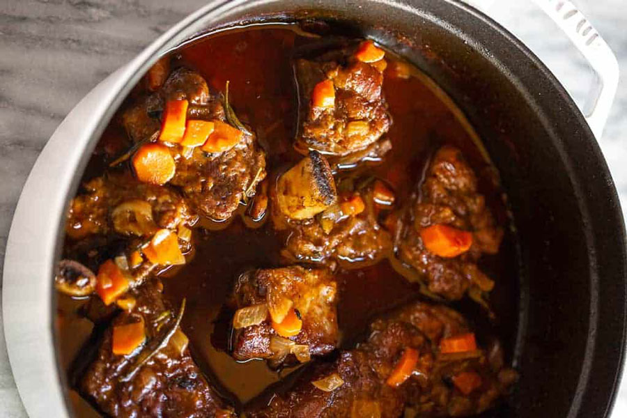 Large pot of prime beef products braised short ribs simmering over kitchen stove.