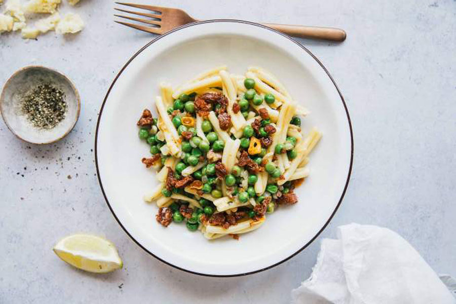 Enjoy a Delectable Spring Pea Pasta with our Mexican Chorizo 1 White bowl with fork and lemon of pasta and crumbled mexican chorizo on top.