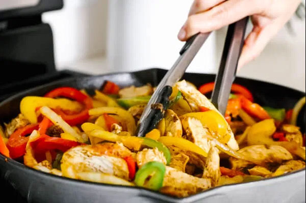 Person using tongs to flip chicken fajitas and vegetables so you can order fajitas online