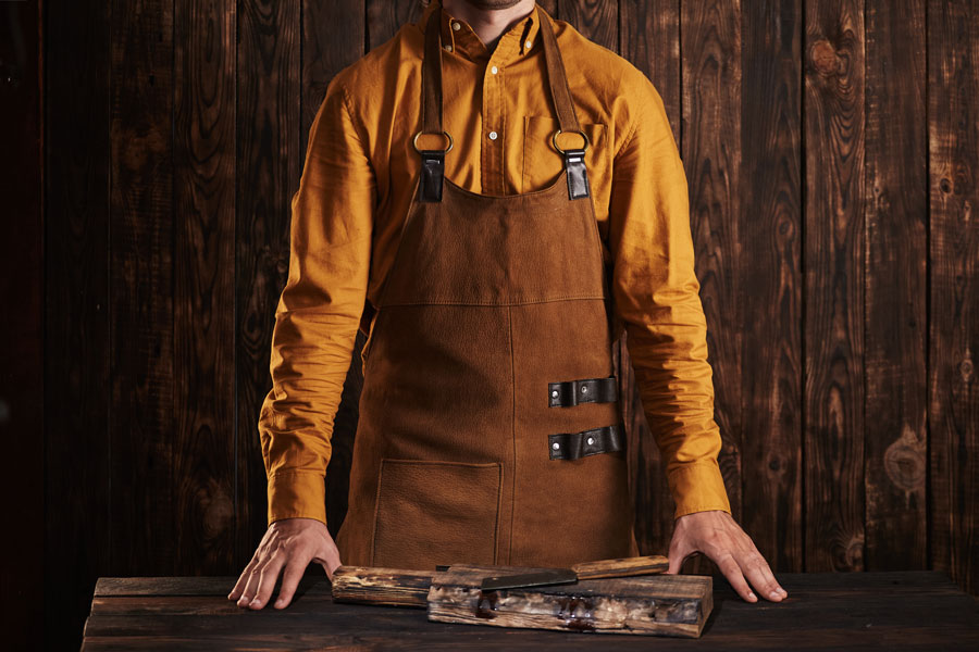 butcher prepping to cook prime steaks in the leather apron put his hands on the wooden table